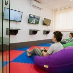 Дети играют в видеоигры на пуфах в игровой комнате санатория «Лесная Песня» в Трускавце