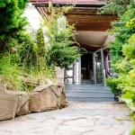 Вхід до вілли Хижина SPA у Трускавці крізь зелені кущі та кам’яні сходи