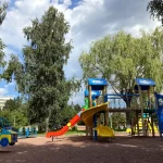 Детская площадка курортного комплекса с горками и качелями на фоне зелени в Трускавце