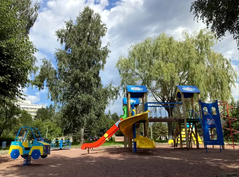 Детская площадка курортного комплекса с горками и качелями на фоне зелени в Трускавце